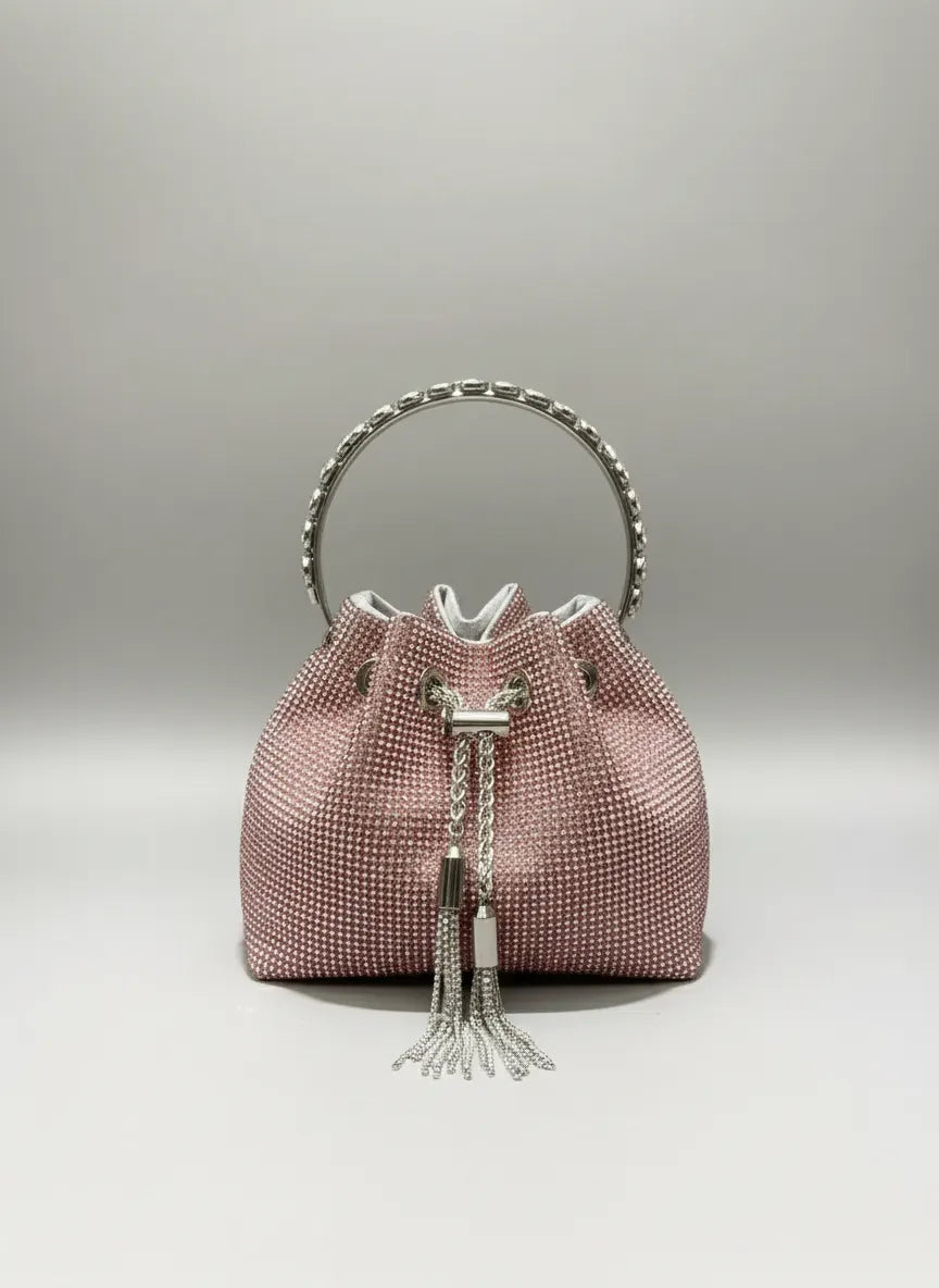 Pink textured handbag with silver handle and tassel on a gray background
