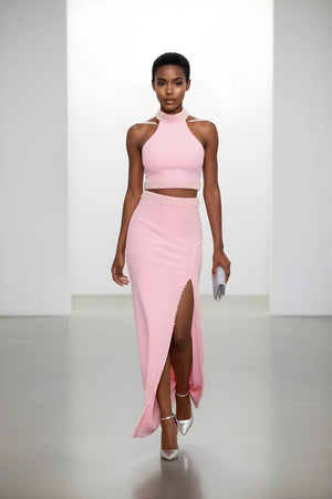 Model wearing a pink high-neck crop top and skirt with a slit on a white background