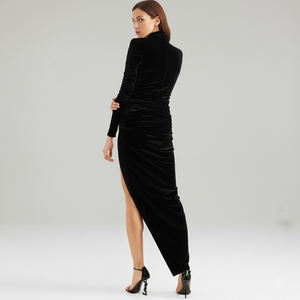 Woman wearing a black velvet dress with a high slit on a gray background
