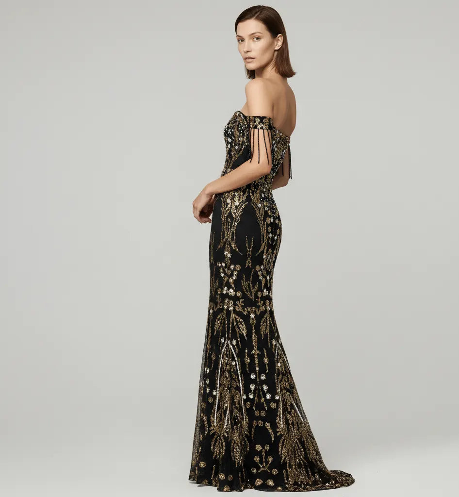 Woman wearing a black and gold evening gown with intricate designs on a gray background