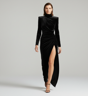 Woman wearing a black velvet dress with a high slit on a gray background