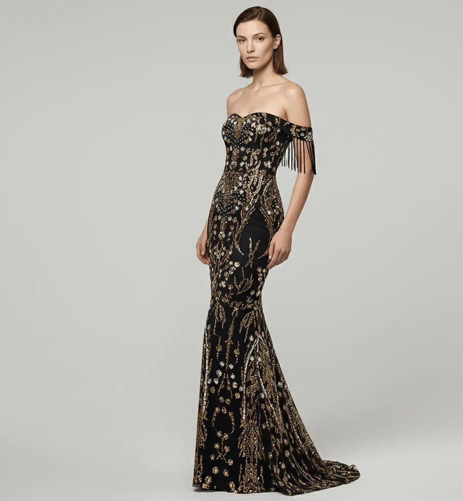 Woman wearing a black and gold evening gown with fringe details on a gray background