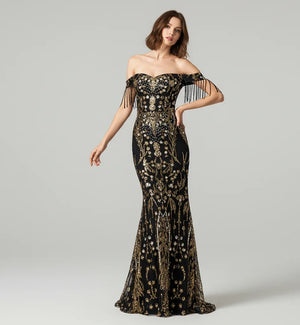 Woman wearing a black and gold evening gown with intricate designs on a gray background