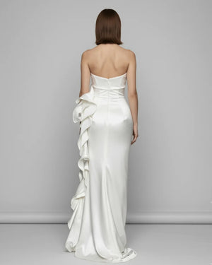 Woman wearing a strapless white wedding dress with ruffles on a gray background