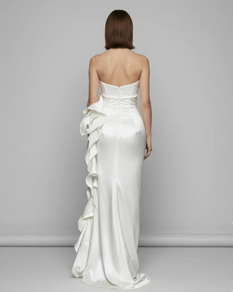 Woman wearing a strapless white wedding dress with ruffles on a gray background