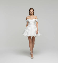 Woman wearing a white off-shoulder dress on a plain background