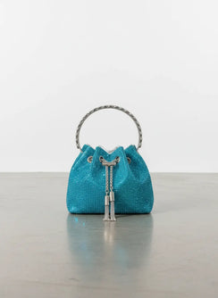 Turquoise woven handbag with silver handle and tassel on a reflective surface.
