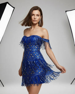 Woman wearing a blue off-shoulder dress with fringe details on a gray background