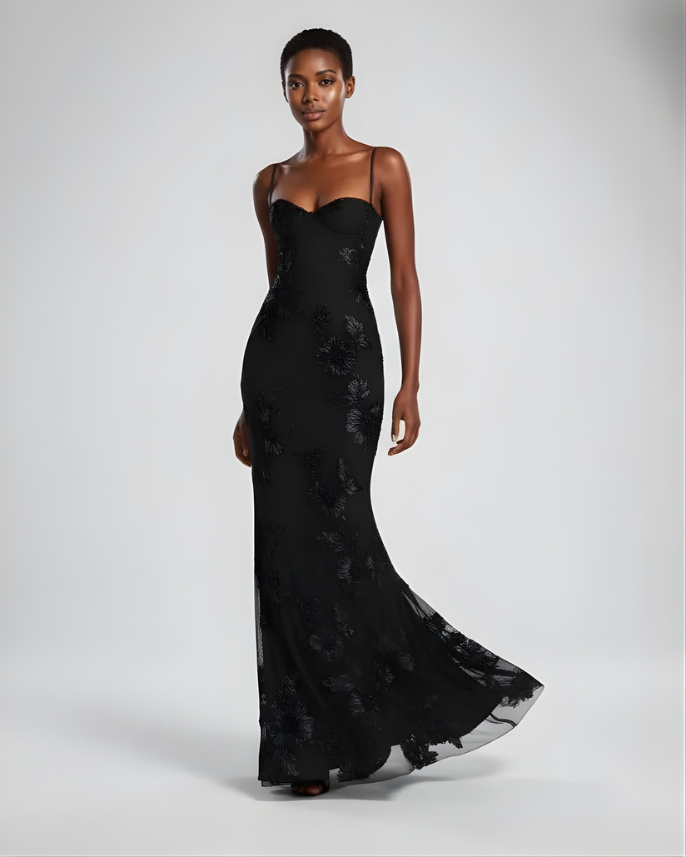 Woman wearing a black evening gown with floral lace details on a white background