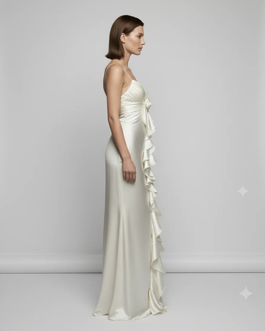 Woman wearing a white evening gown with ruffled details on a plain background