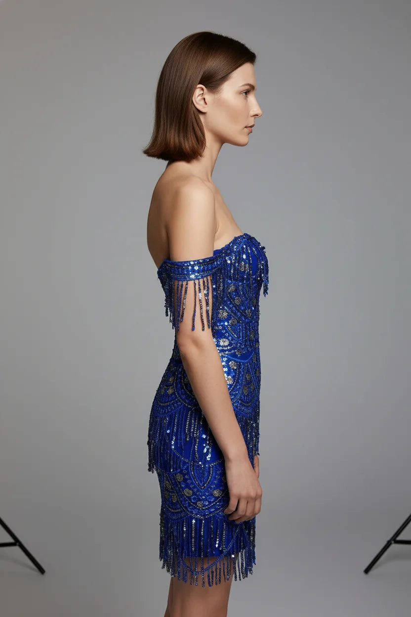 Woman wearing a blue sequin dress with fringe details on a gray background