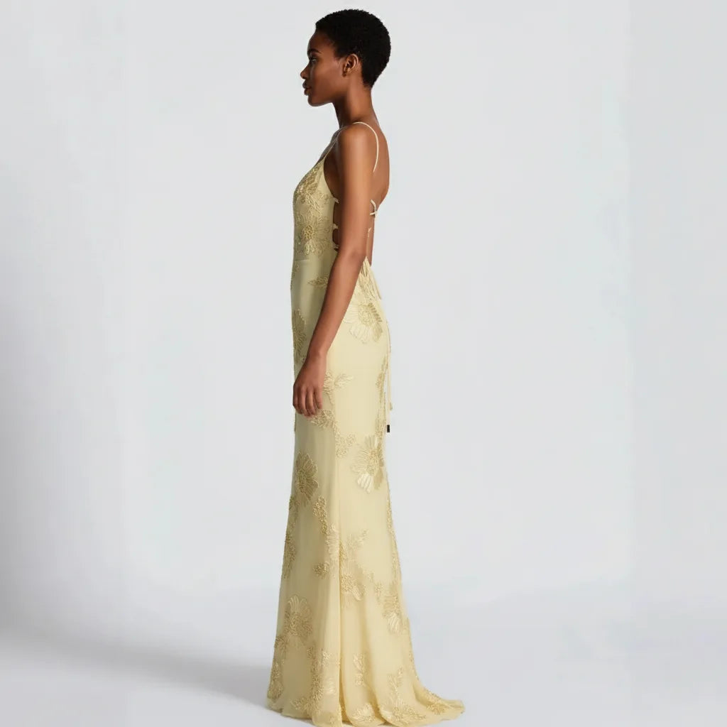 Woman wearing a long, light-colored lace dress against a plain background