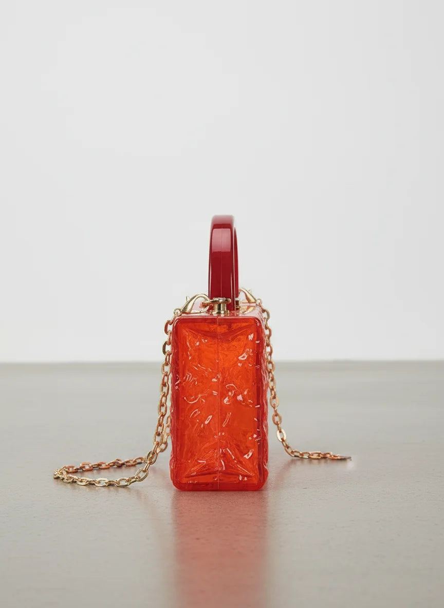 Orange handbag with chain strap on a light gray surface and background