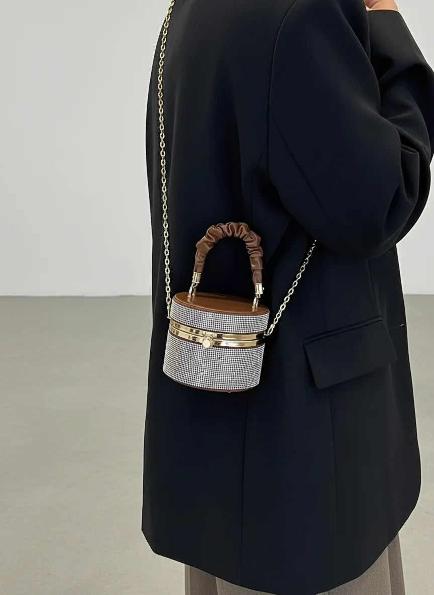 Person wearing a black coat with a small handbag featuring a chain strap and wooden handle.